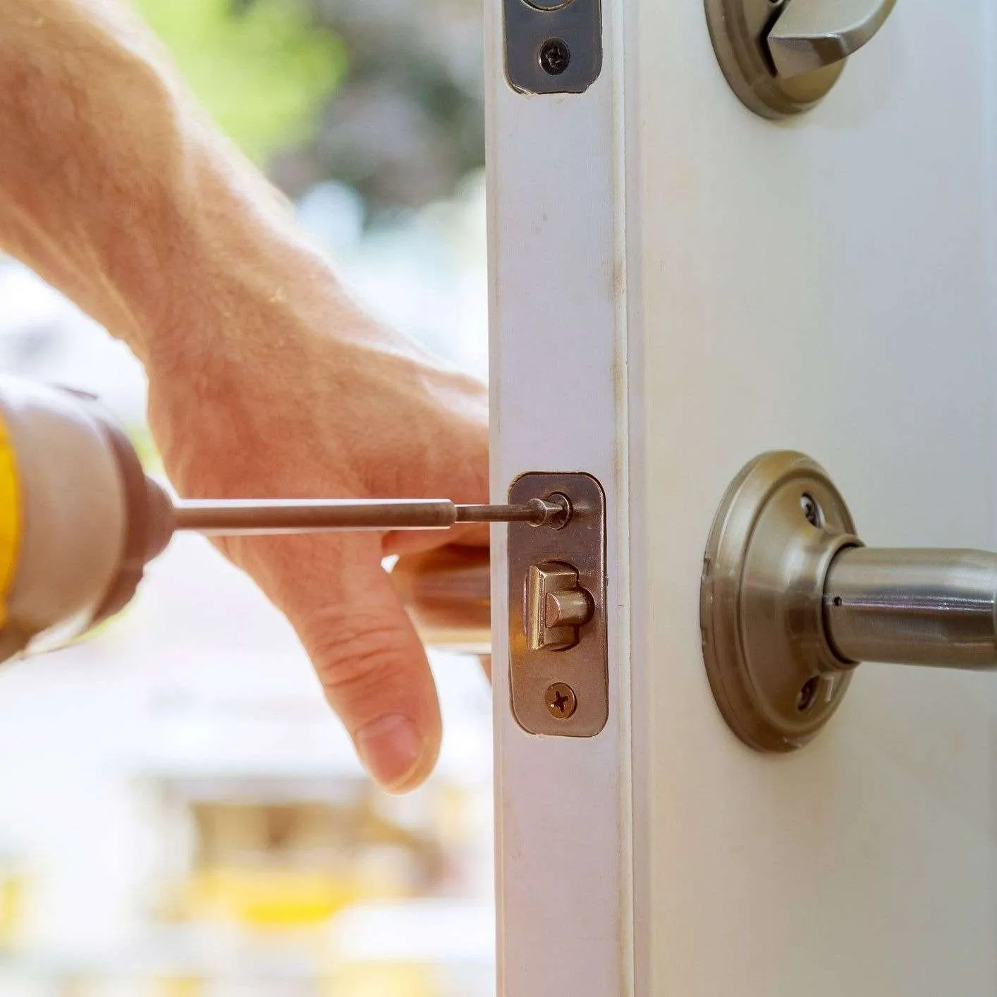 Hand using screwdriver on door lock mechanism.