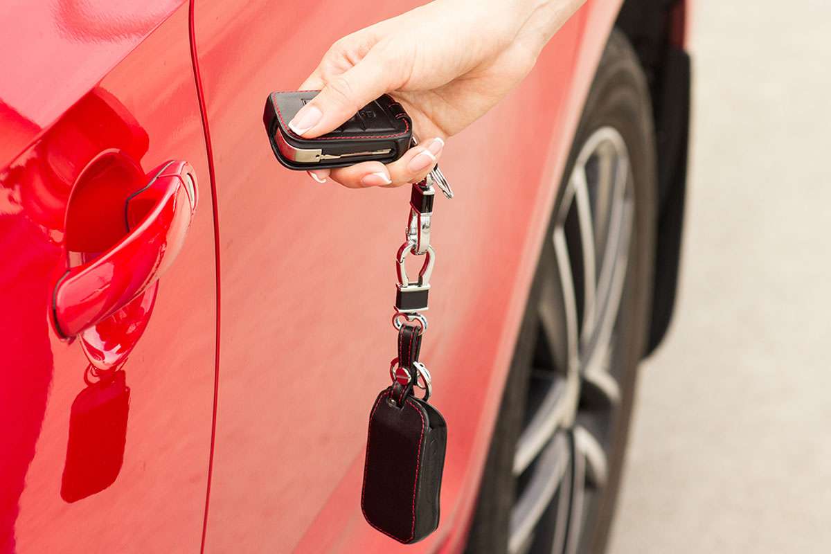 Hand holding car keys near red vehicle door.